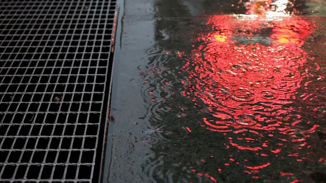 雨水洒在人行道上，折射着霓虹灯
