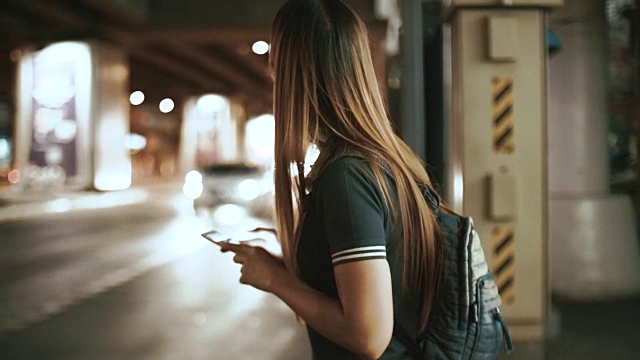 亚洲女性在晚上用智能手机请求和等待优步