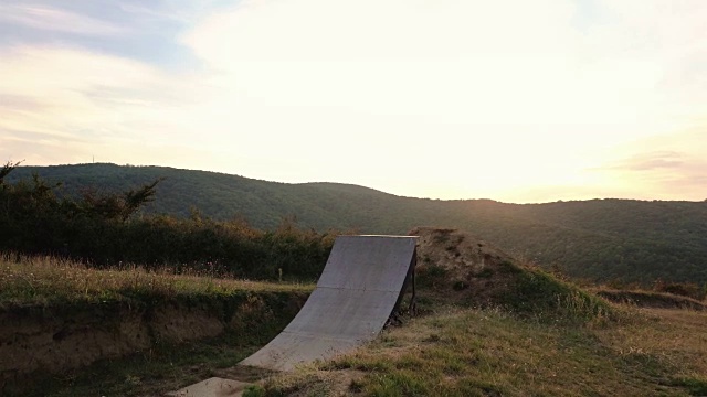 极限自行车选手跳过运动坡道，在日落时向后翻泥山。