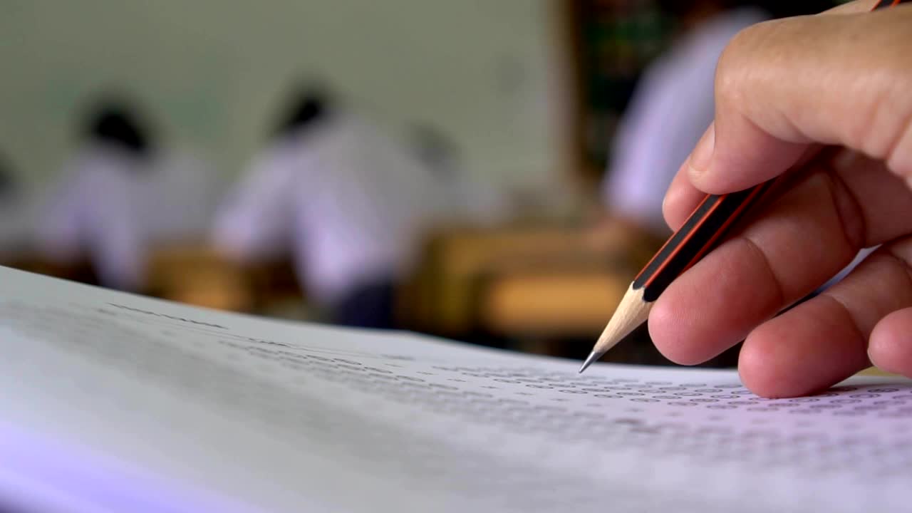 教育考试概念:高中课堂上，学生手持考笔，写答题卡或练习题，在木桌上用复写纸电脑答题