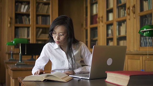 勤奋的女学生生物学家在桌子上写书和笔记本电脑在图书馆