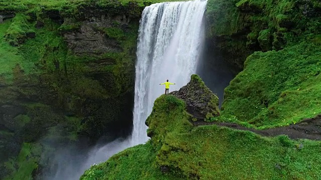 在冰岛，一名男子双手高举在山顶，站在瀑布前庆祝旅行和冒险