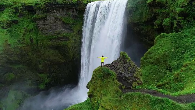 詳情圖-在冰島，一名男子雙手高舉在山頂，站在瀑布前慶祝旅行和冒險