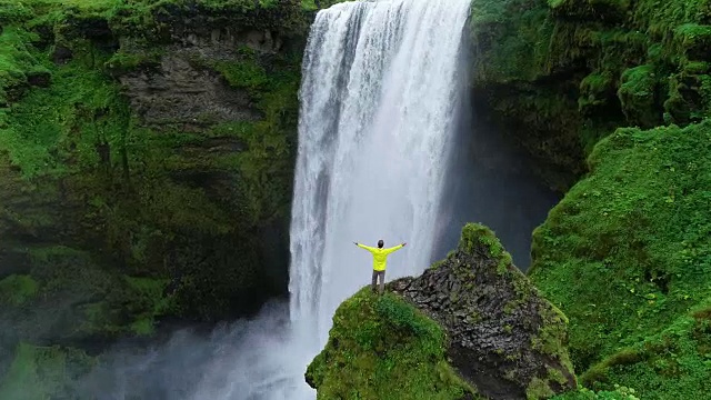 詳情圖-在冰島，一名男子雙手高舉在山頂，站在瀑布前慶祝旅行和冒險