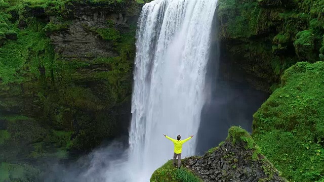 詳情圖-在冰島，一名男子雙手高舉在山頂，站在瀑布前慶祝旅行和冒險