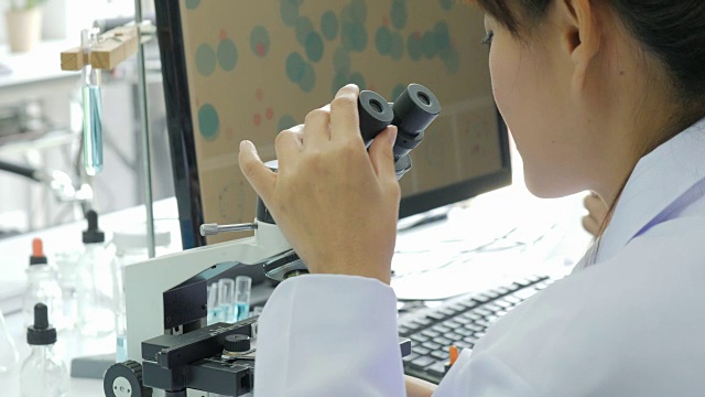 在实验室里通过显微镜观察的亚洲女性医学研究科学家