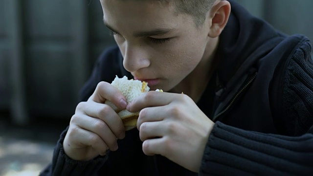 饥饿的少年吃着便宜的不健康的三明治，劣质的儿童餐