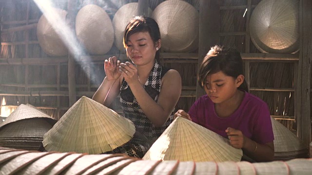 两名同胞越南工匠在老传统房子制作传统越南帽子的4k镜头低光场景，在Ap Thoi Phuoc村，Cantho省，越南，传统艺术家的概念