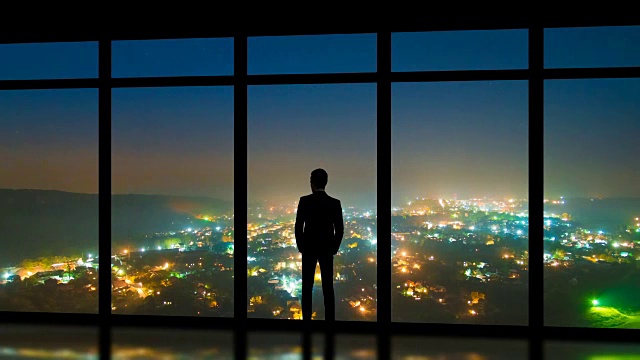 詳情圖-這個男人站在全景窗戶旁，以霧蒙蒙的城市為背景。時間流逝