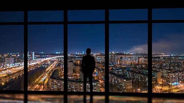 详情图-这个男人站在窗户旁边，背景是夜晚的大都市。时间流逝