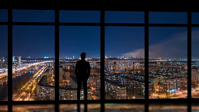 详情图-这个男人站在窗户旁边，背景是夜晚的大都市。时间流逝