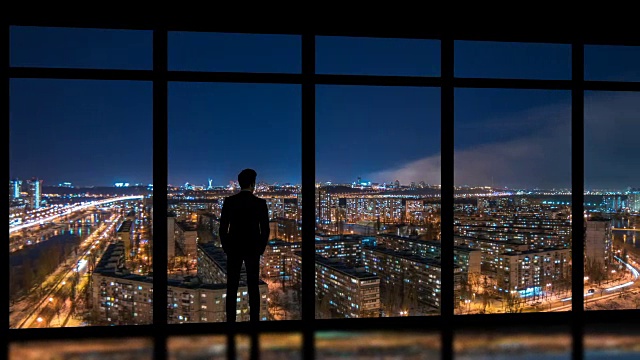 详情图-这个男人站在窗户旁边，背景是夜晚的大都市。时间流逝
