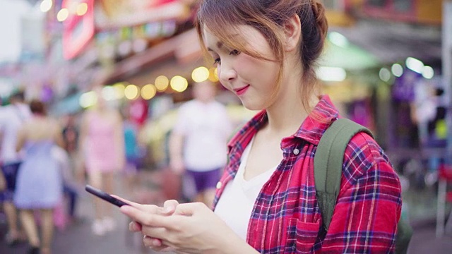 详情图-亚洲女性背包客微笑和使用智能手机独自旅行户外在曼谷考山路的城市街道，曼谷-泰国。