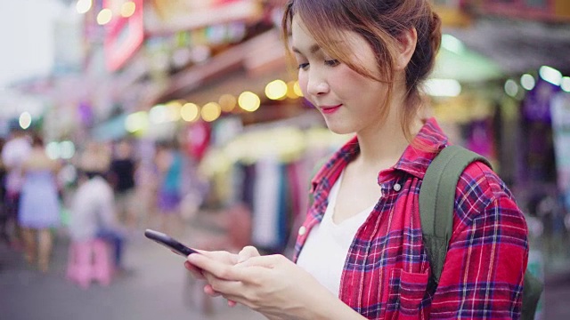 详情图-亚洲女性背包客微笑和使用智能手机独自旅行户外在曼谷考山路的城市街道，曼谷-泰国。
