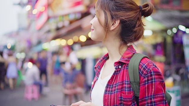 详情图-亚洲女性背包客微笑和使用智能手机独自旅行户外在曼谷考山路的城市街道，曼谷-泰国。