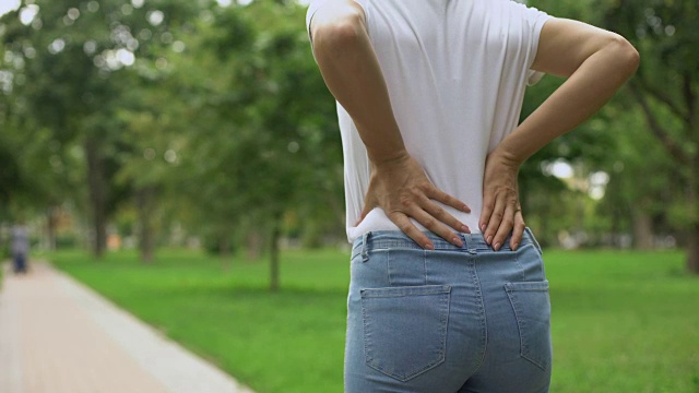 苗条的女人在公园散步，感觉背疼不舒服，风湿，保健