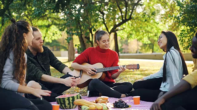 詳情圖-當(dāng)美麗的年輕女子在公園野餐時，歡快的人們唱歌和大笑的慢鏡頭。音樂，休閑和樂趣的概念。