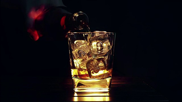 詳情圖-酒保將威士忌倒入裝有冰塊的玻璃杯中，放置在木桌和黑色的背景上，重點放在冰塊上，威士忌放松的時間放在溫暖上