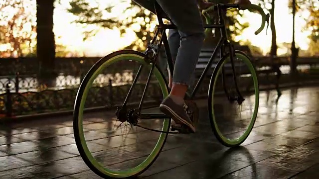 詳情圖-女性的腳在早上的公園或大道騎自行車的近鏡頭。側(cè)面的一個(gè)年輕女子騎著一輛徒步自行車，穿著運(yùn)動(dòng)鞋和牛仔褲。陽(yáng)光照在背景上