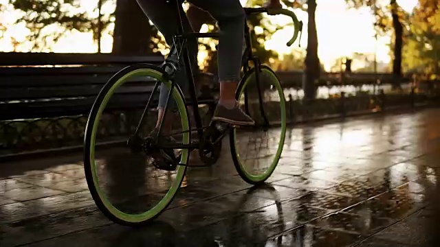 詳情圖-女性的腳在早上的公園或大道騎自行車的近鏡頭。側(cè)面的一個(gè)年輕女子騎著一輛徒步自行車，穿著運(yùn)動(dòng)鞋和牛仔褲。陽(yáng)光照在背景上