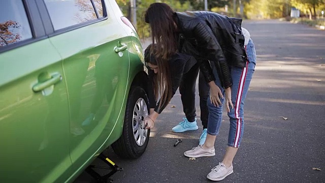 在乡村的土路上，两名妇女用千斤顶把一辆汽车抬起来，然后换瘪胎