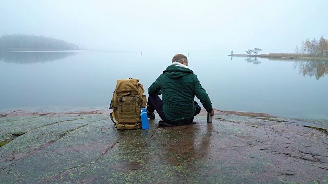 一个背着背包的中年男子坐在波罗的海的岩石海岸上。