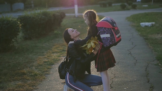 一个女人在学校见她的小女儿。一个穿着校服背着背包的女孩拥抱和亲吻她的妈妈。慢动作