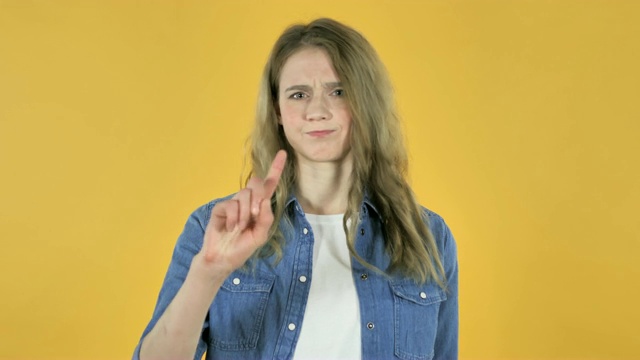 年轻漂亮的女孩挥舞手指拒绝黄色背景