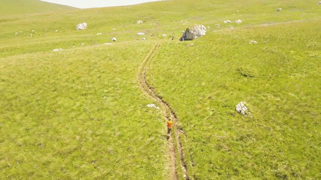 年轻人在夏季草地上奔跑在高山高地鸟瞰图