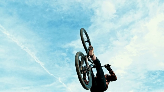 在蓝天白云的映衬下，年轻男子跳跃和后空翻BMX自行车