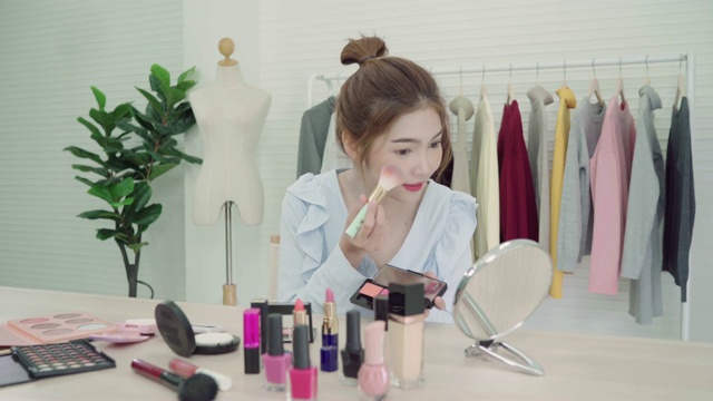 美妆博主坐在镜头前拍摄美妆视频。美丽的亚洲女性一边化妆一边复习化妆教程，由互联网在社交网络上直播。