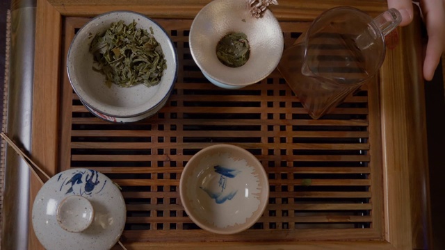 师傅从盖湾的茶壶里倒热水，茶几上放绿茶