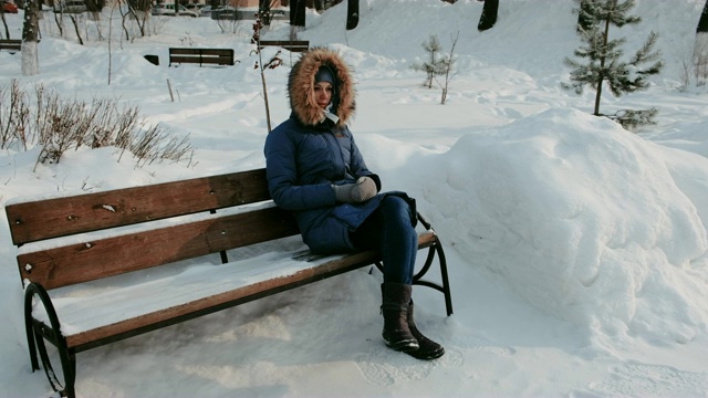 一个女人坐在冬天城市公园的长椅上，在下雪的天气里。