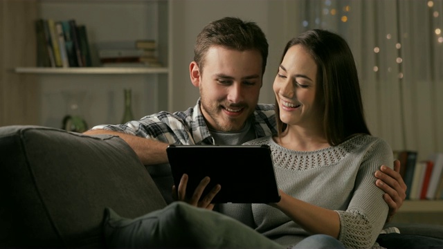 新婚夫妇在晚上浏览平板电脑上的内容
