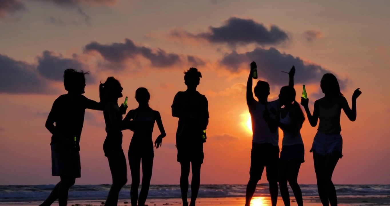 一群朋友在海滩上玩和喝酒的剪影。假期——iStock