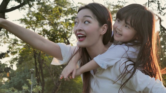 生活方式的母亲和女儿在幸福的在野外在日落的光。家人在做节日活动。亚洲家庭在花园里玩耍。幸福的家庭的概念。放松的育儿