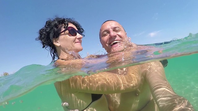 幸福浪漫的情侣对着相机微笑，在夏天的海滩度假，gopro圆顶半水下的景色，慢镜头