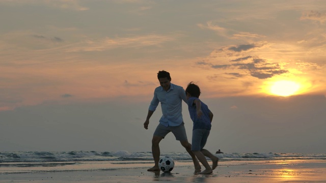 詳情圖-亞洲父親和兒子一起在沙灘上玩足球在夕陽的背景下。緩慢的運動。幸福的家庭的概念。