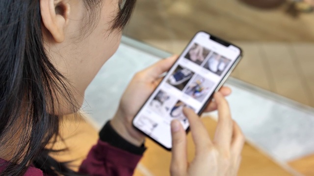 女人在网上服装店看商品，智能手机网上购物，慢镜头。