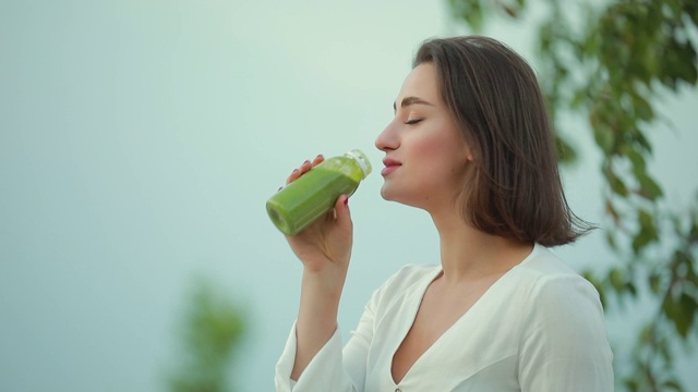 美丽的女人在户外喝绿色冰沙