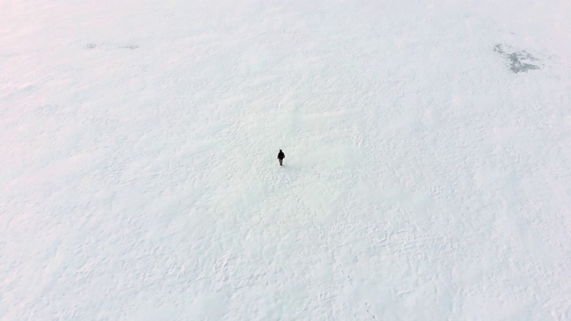 一个人走在雪地上的空中盘旋镜头。