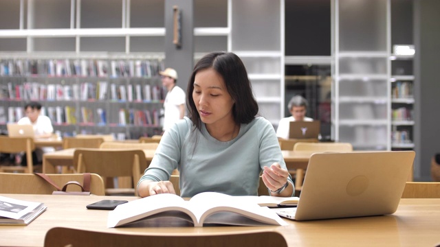 亚洲女学生使用智能手机进行图书馆教育，阅读书籍和做笔记
