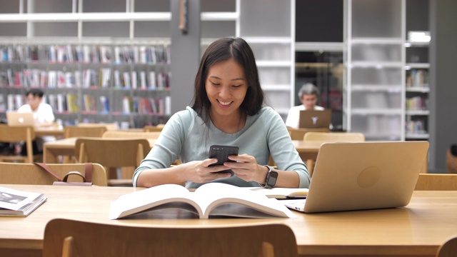 詳情圖-亞洲女學生使用智能手機進行圖書館教育，閱讀書籍和做筆記