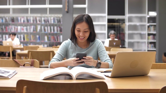 詳情圖-亞洲女學生使用智能手機進行圖書館教育，閱讀書籍和做筆記