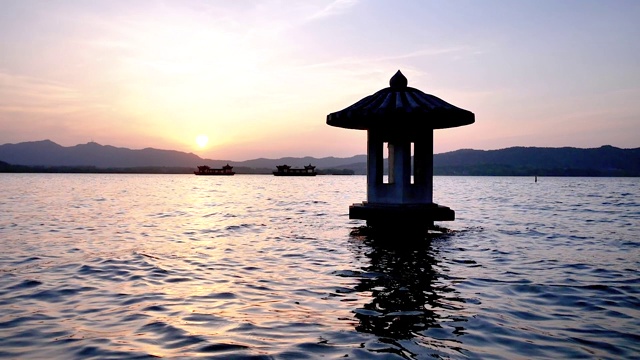 美丽的日落风景在西湖，中国，杭州，橘色的黄昏天空和宁静的水与传统的亭台楼阁在湖中，闪烁的涟漪，超级慢的动作。