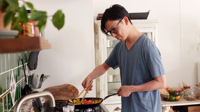 詳情圖-(中景)一個年輕人在家里一邊看電子平板電腦一邊做飯