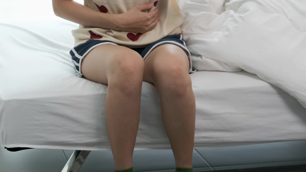亚洲女性早上在卧室床上醒来时会胃痛
