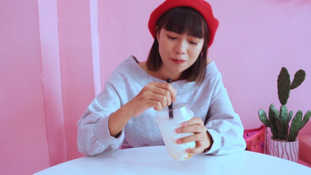 年轻的亚洲千禧一代女性在粉色柔和的咖啡馆喝冰珍珠奶茶