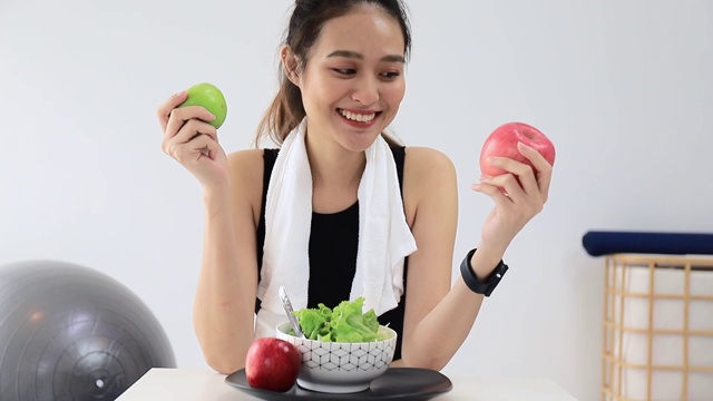 美丽的亚洲女人健康的博主展示了苹果水果和干净的减肥食品。在摄像机前录制在家的视频直播。在线社交媒体上的健身影响者。