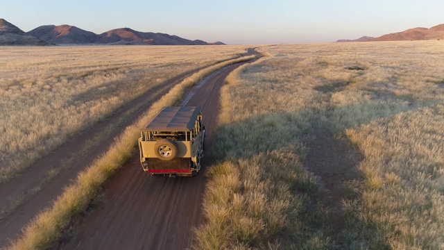 4K高的空中后视图，一辆4x4旅行车辆驾驶在沙地上通过非洲大草原与著名的仙女圈，纳米比亚